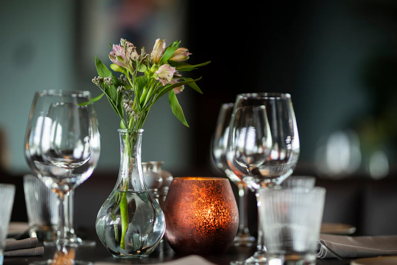 Et vakkert dekket bord med en vase med blomster, et glødende lys og glitrende glass, klart for et måltid.