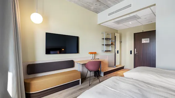 A modern hotel room with two beds, a desk area, and a TV, designed for comfort and functionality.