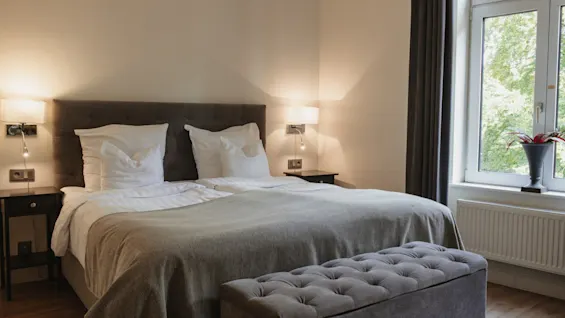 Et komfortabelt hotelværelse med en stor seng, sengebelysning og et vindue med udsigt til træer. Home Hotel Norre Park i Halmstad.