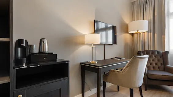 Et velindrettet hotelværelse med skrivebord, stol, tv og kaffestation, der tilbyder komfort og bekvemmelighed.