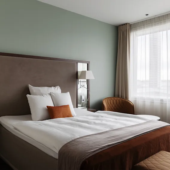 Ett välkomnande hotellrum med en bekväm säng, eleganta möbler och ett stort fönster som ger gott om ljus.