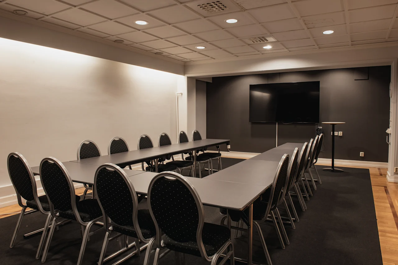Ett modernt konferensrum på Home Hotel Grand, Helsingborg, med ett U-format bord, stolar och en stor skärm för presentationer.