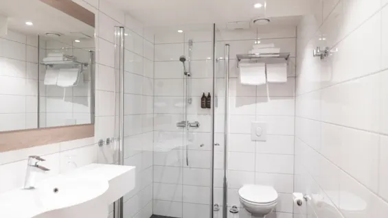 Et rent og moderne hotellbad med vask, speil, dusj og toalett, klart til bruk.