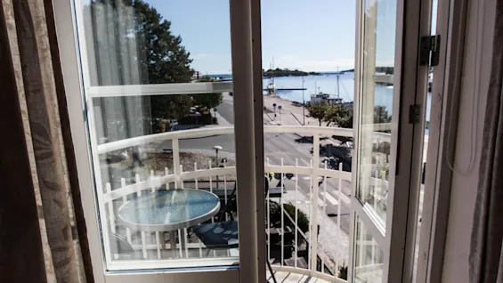 Open balcony doors overlooking a sunny harbor with a small balcony table and chairs.
