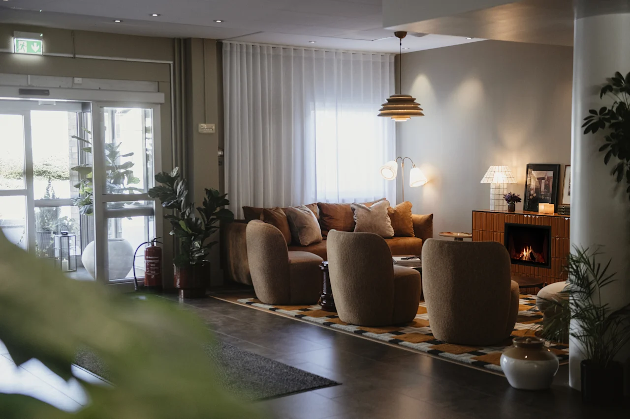 En inbjudande hotellounge med en varm öppen spis, plyschmöbler och rikligt med naturligt ljus, vilket skapar en mysig atmosfär.