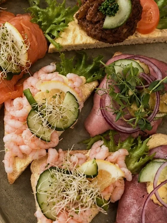 Et fat med snitter pyntet med røkt laks, reker, roastbiff, agurk og friske spirer.
