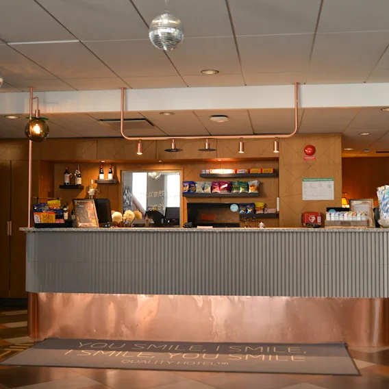 Reception desk with snacks and drinks displayed, located in a well-lit lobby with modern decor. Text on floor mat: "YOU SMILE I SMILE".