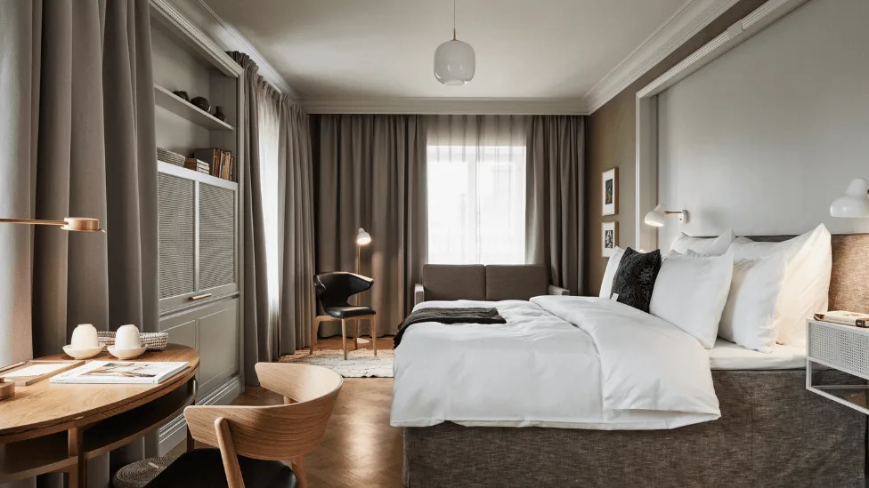 Stilfuldt hotelværelse med nyredt seng, træmøbler og hyggelig belysning; varm og indbydende atmosfære.