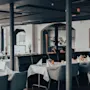 En modern restaurangmiljö med dukade bord, vita dukar och eleganta mörka stolar.