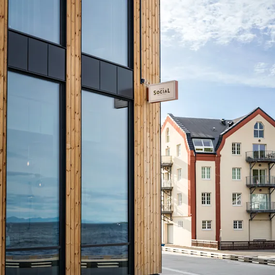 Moderne bygning med store vinduer mot havet, med et 'Social'-skilt, en del av Quality Hotel Harstad.