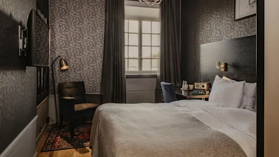 Ett välutrustat hotellrum på Home Hotel Grand, Helsingborg, redo för en bekväm vistelse med säng, skrivbord och naturligt ljus.