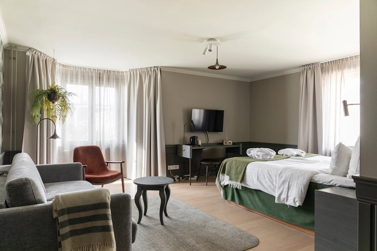 Kutsuva hotellihuone, jossa on mukava sänky, viihtyisä oleskelualue ja toimiva työpiste valoisan ikkunan äärellä.
