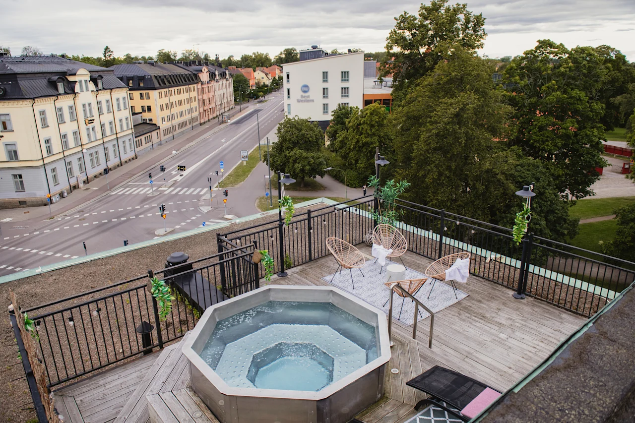 Rooftop terrace with a bubbling hot tub and comfortable seating, overlooking a city street and buildings.
