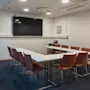 A modern conference room at Home Hotel Uppsala with a U-shaped table, chairs, a large screen, and a whiteboard, ready for a meeting.