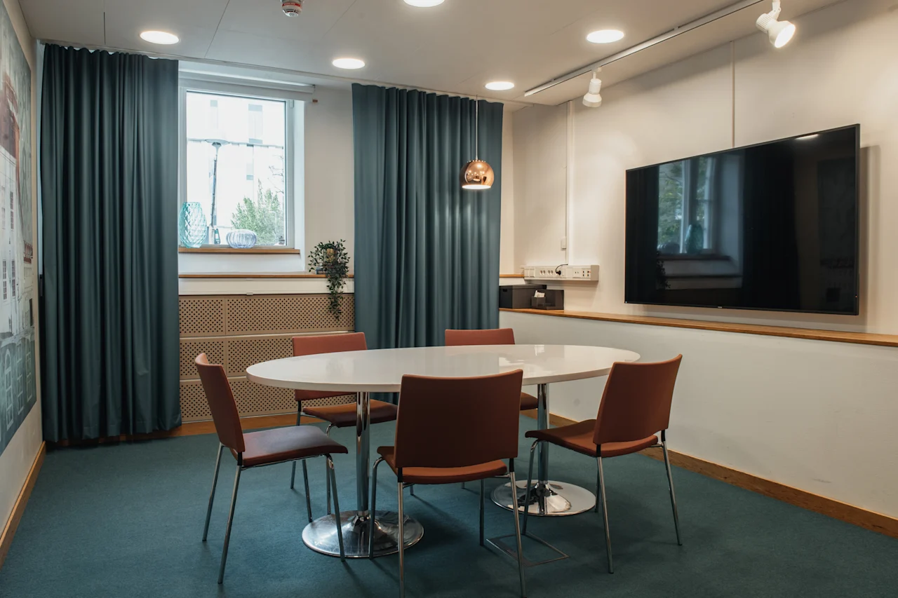 A cozy meeting space at Home Hotel Uppsala, featuring an oval table, comfortable chairs, and a large screen for presentations.