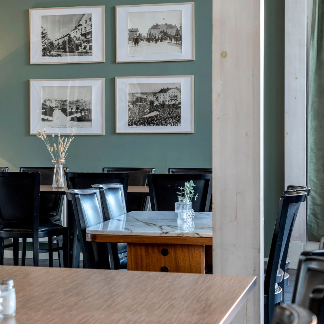Wooden tables and metal chairs in an empty café, with framed photographs on a green wall.