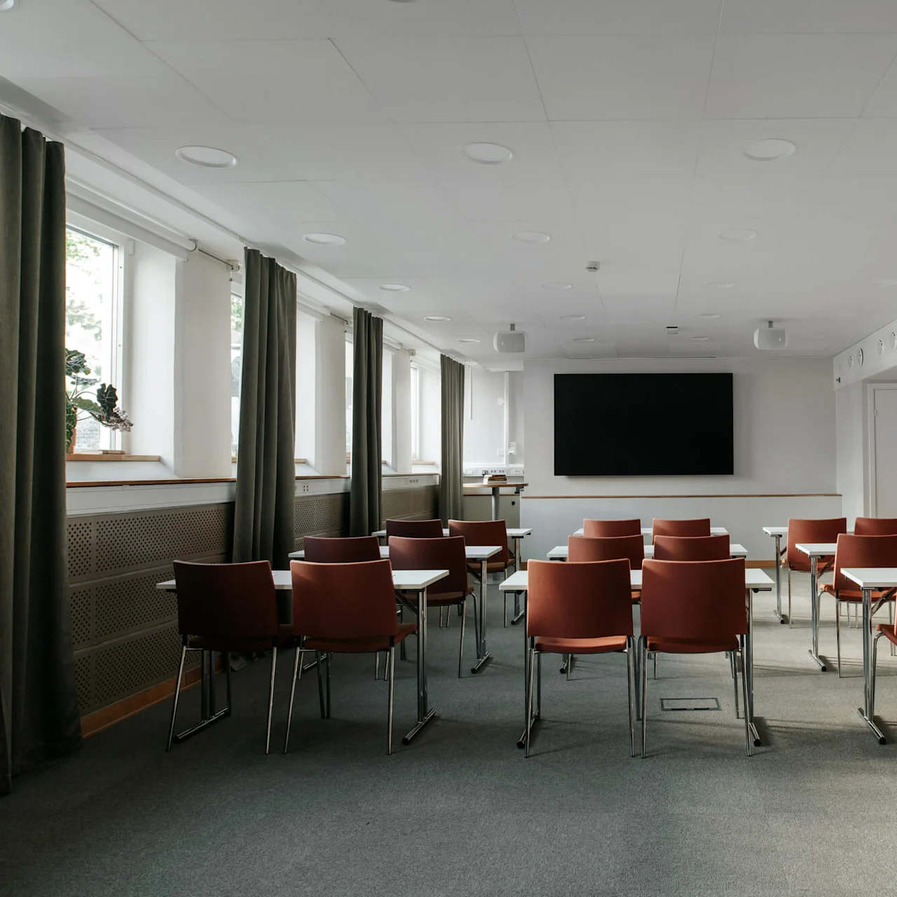 Rows of brown chairs facing a large blank screen in a well-lit, empty conference room.