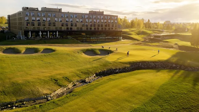 Golfers play on a course near a modern building bathed in sunset light.