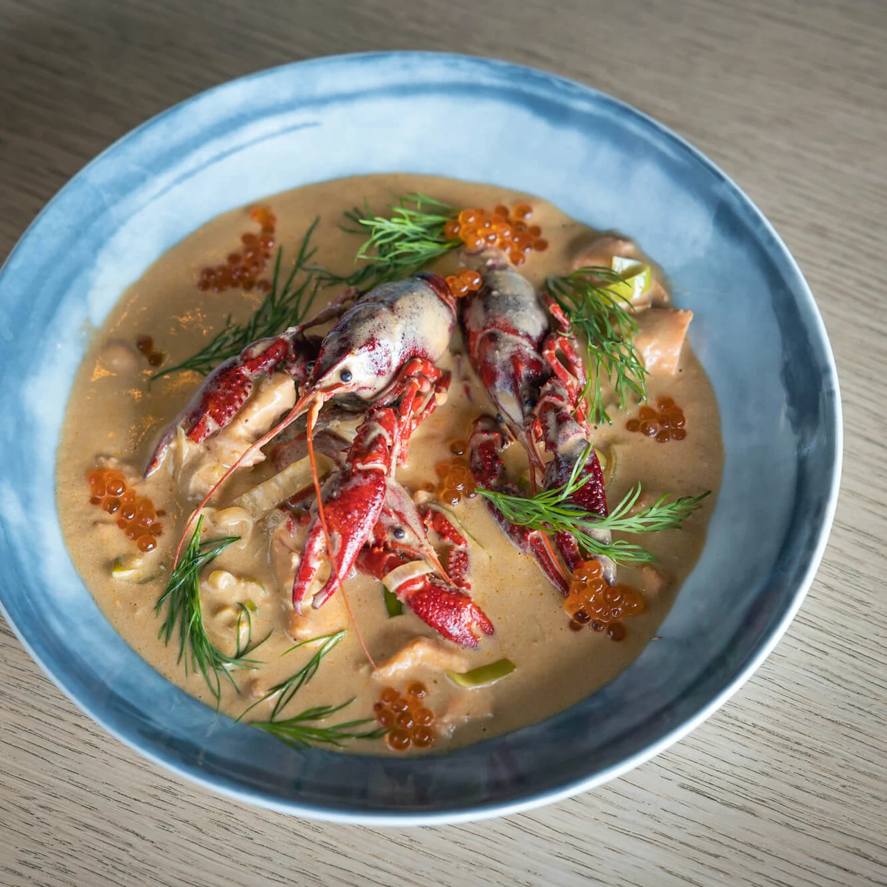 Krebs og dild pryder en skål med cremet suppe, spredte fiskeæg på et træbord.