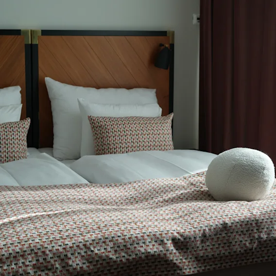 En hyggelig hotelseng med hvide puder, mønstrede pynteputer og en rund dekorativ pude.