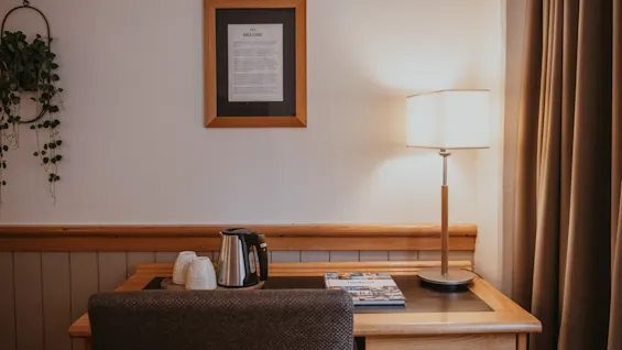A cozy desk area with a kettle, cups, and a lamp, featuring a framed document titled THE MENU.