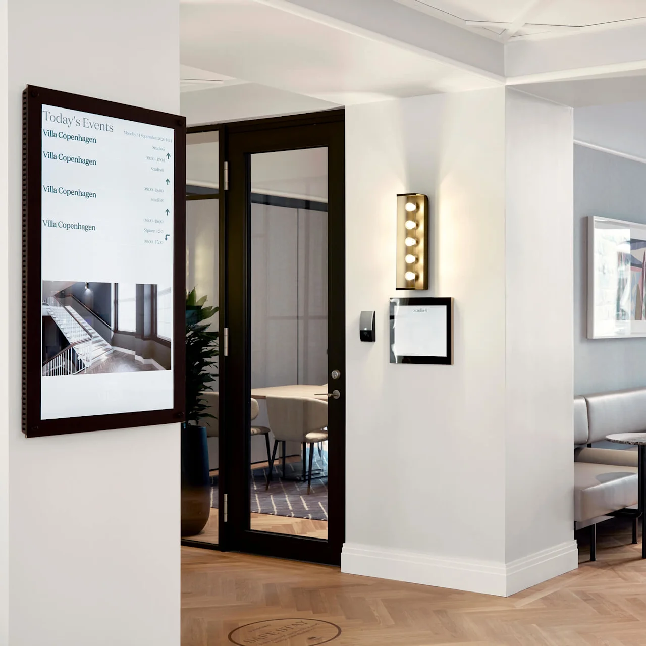 Digital sign displaying “Today's Events,” listing events at Villa Copenhagen; modern interior with a seating area and glass door leading outside.
