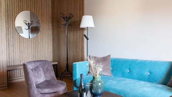 Modern sittgrupp i hotellrum med blå sofa, fåtölj och träpaneler på väggen.