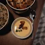 En bolle kremet suppe med krutonger og en skje, akkompagnert av boller med frø og flere krutonger på et trebord.