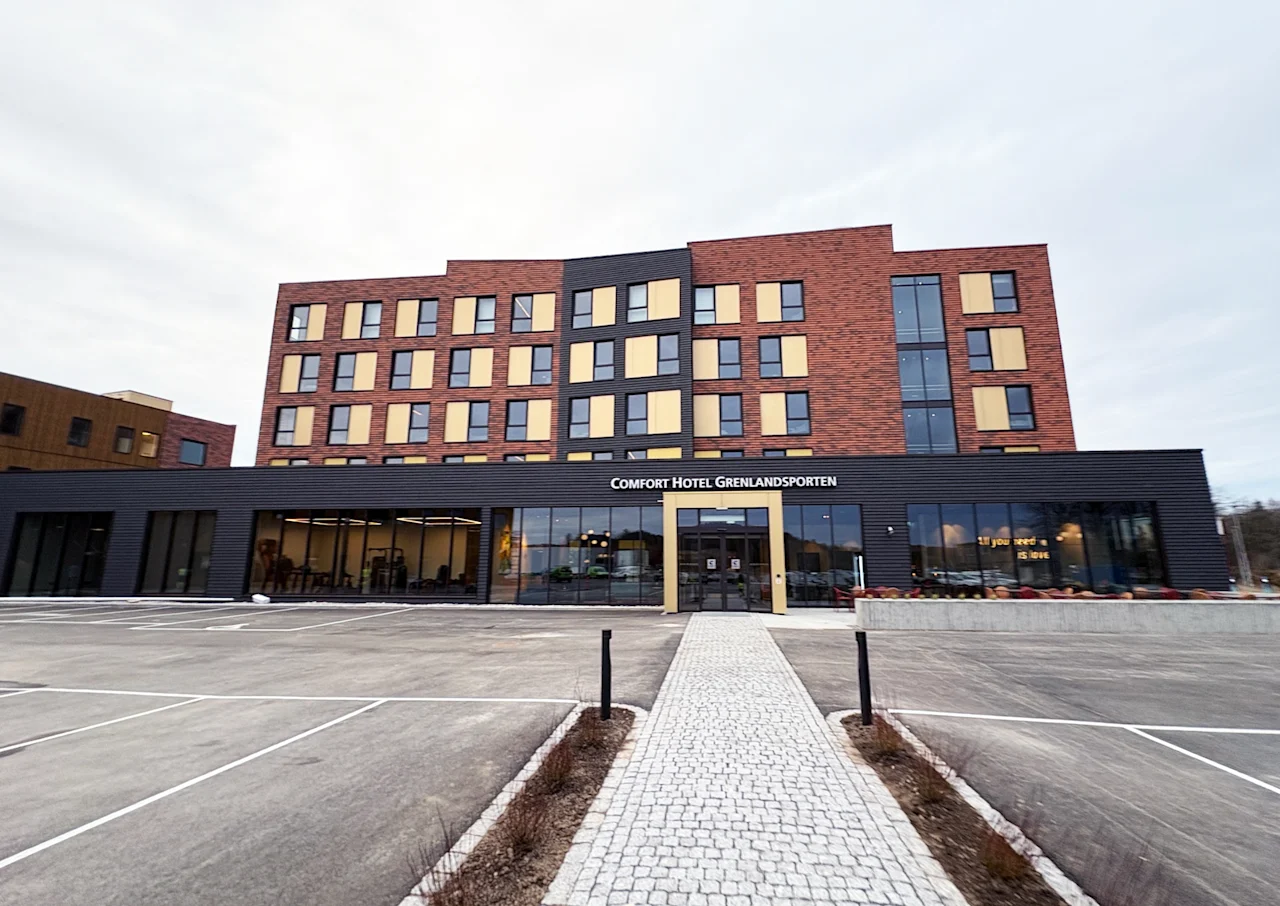 Moderne hotellbygning med stor parkeringsplass og gangvei. Tekst på bygget: Hotel Grenlandsporten. 