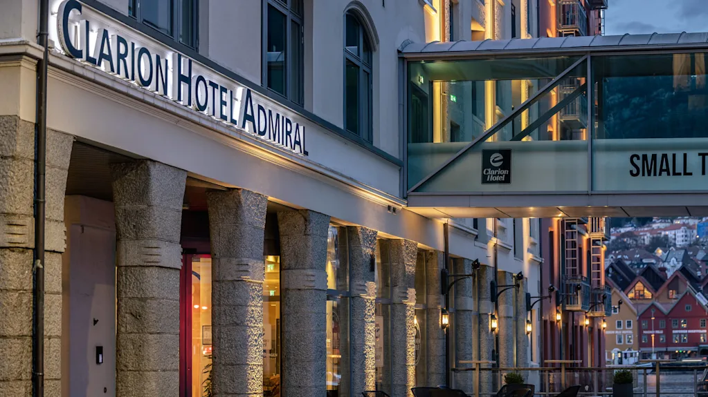 Clarion Hotel Admiral-entré under en täckt gångbro, med en skylt som lyder "SMALL TALK". Sittplatser och utomhusbelysning skapar en inbjudande kvällsatmosfär.