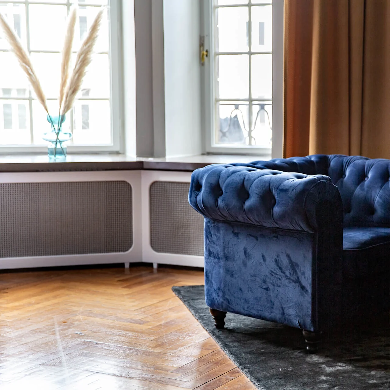 To komfortable blå sofaer er plassert mot hverandre i en stilfull stue, med naturlig lys som filtreres gjennom et vindu med gardiner.