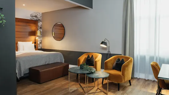 Et stilfuldt hotelværelse designet til afslapning, med en komfortabel seng og et indbydende siddeområde med to bløde lænestole.
