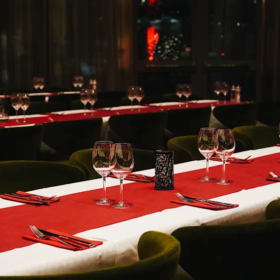 Lange middagsbord dekket med hvite duker, røde løpere, vinglass og bestikk i en restaurant.