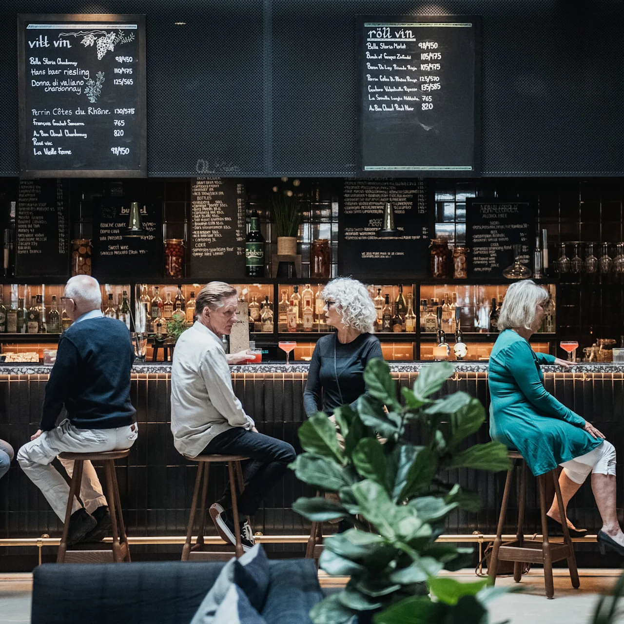 People conversing at a bar with drinks, in a sophisticated setting with menus on blackboards.