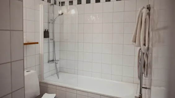 Et rent og funktionelt badeværelse med badekar og bruser, et toilet og friske håndklæder hængende på en opvarmet håndklædeholder.