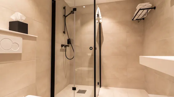 Et rent, moderne bad med en dusj i glass, toalett og vaskeområde, med friske håndklær og en tørkepapirboks.