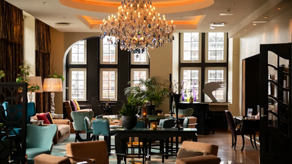 Luksuriøs lysekrone som lyser opp en koselig lounge dekorert med sofaer, stoler og bord; omgitt av store vinduer og elegant innredning, som skaper en eksklusiv, innbydende atmosfære.