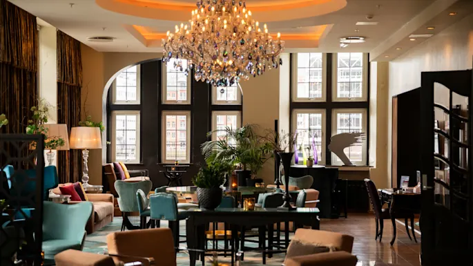 Luxurious chandelier illuminating a cozy lounge adorned with sofas, chairs, and tables; surrounded by large windows and elegant decor, creating an upscale, inviting atmosphere.