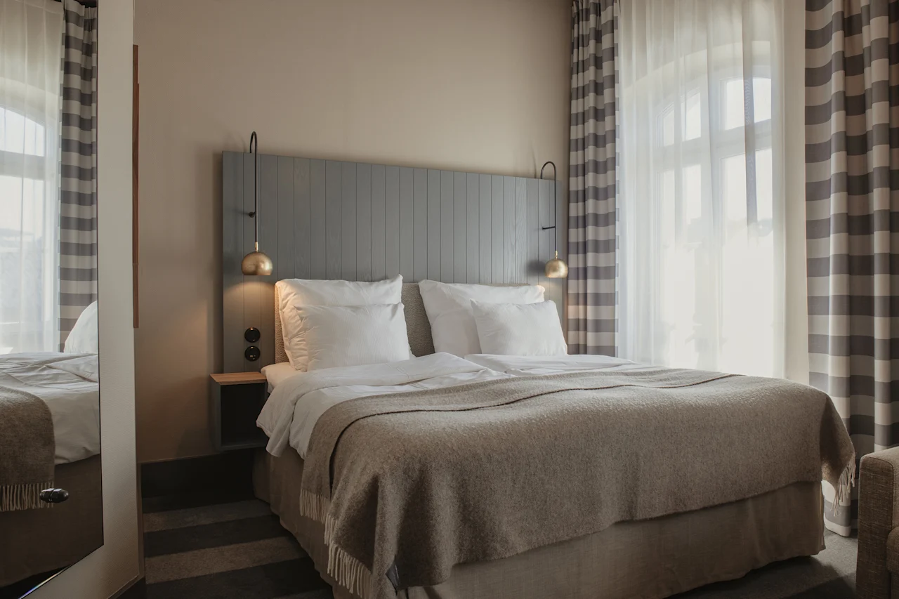 A cozy hotel room with a neatly made bed, bedside lamps, and striped curtains, ready for a comfortable stay.