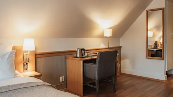 A cozy room with a bed, a desk with a chair, and warm lighting, perfect for relaxation or work.