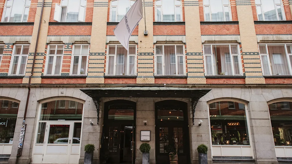 En fleretagers bygning med murstens- og stenfacade, med en fremtrædende indgang med markise og et flag, der viser HOME HOTEL.