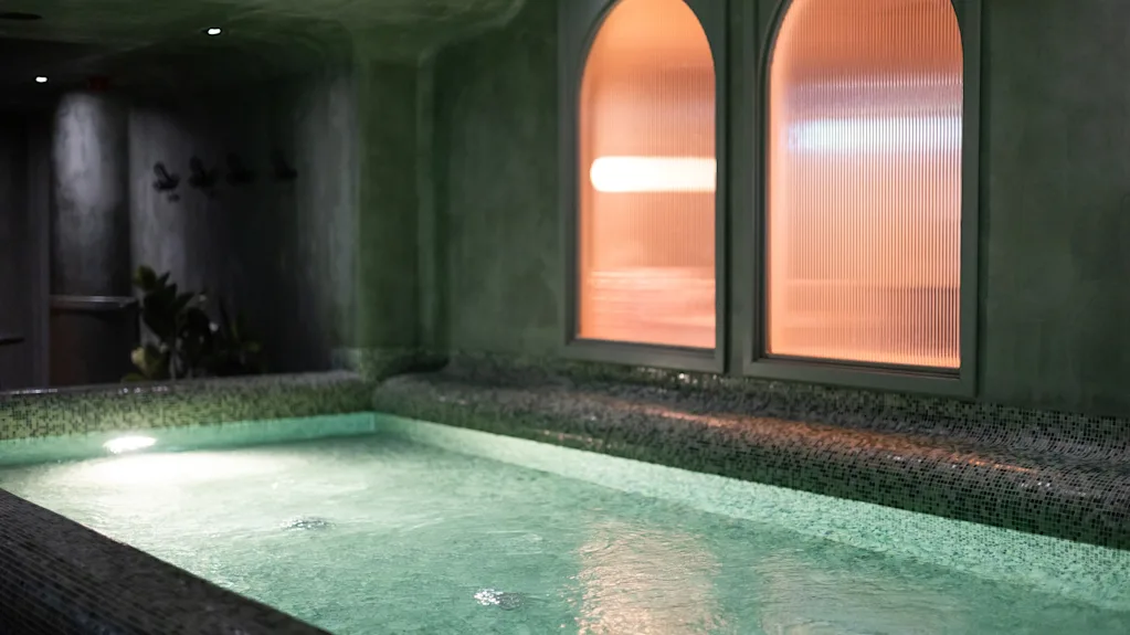 Rauhallinen sisäuima-allasalue porealtaalla ja lämpimästi hehkuvilla kaarevilla ikkunoilla, kutsuen rentoutumaan ja rauhoittumaan.