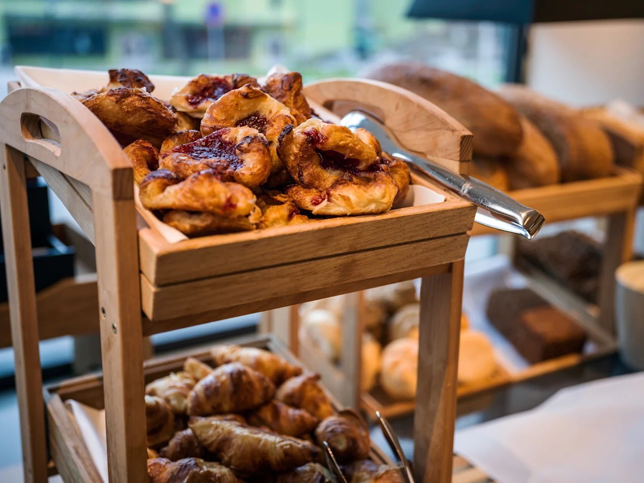 A wooden display stand filled with delicious pastries and bread, including jam-filled danishes and flaky croissants.