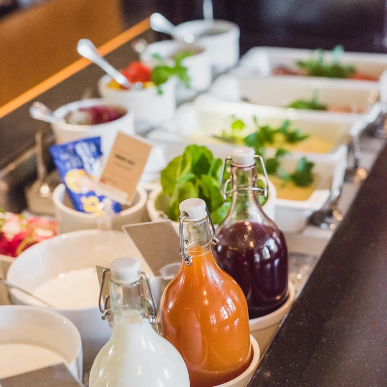 A variety of breakfast items are displayed on a counter with bottles of milk and juice in focus.