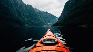 Kayak floating on a fjord between high green mountains
