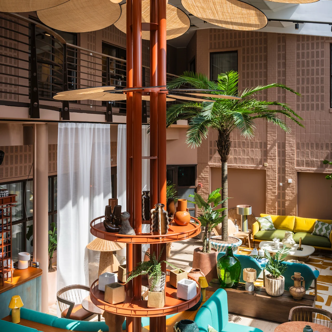A multi-layered wooden shelf holds various decorative items in a vibrant, modern lounge with teal seating, tropical plants, and large leaf-shaped ceiling decor under a glass roof. 
