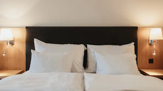 A comfortable hotel bed with crisp white linens, a dark headboard, and warm lighting from bedside lamps.