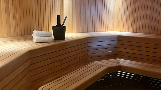 Et koselig badstuerom i tre med benker, en bøtte og håndklær, klart for en avslappende velværeopplevelse.