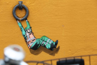 Tegnet mann henger fra ring i veggen som gatekunst i Stavanger
