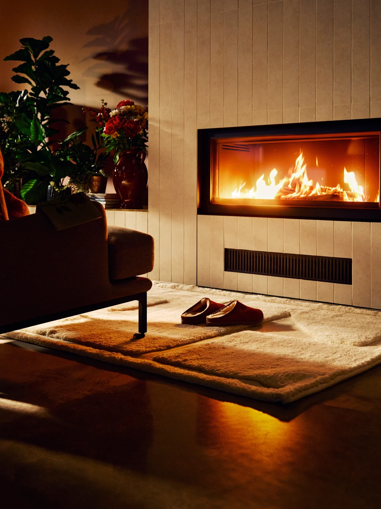 Mysigt vardagsrum med varm öppen spis, inbjudande fåtölj med filt och tofflor på mjuk matta, perfekt för avkoppling.